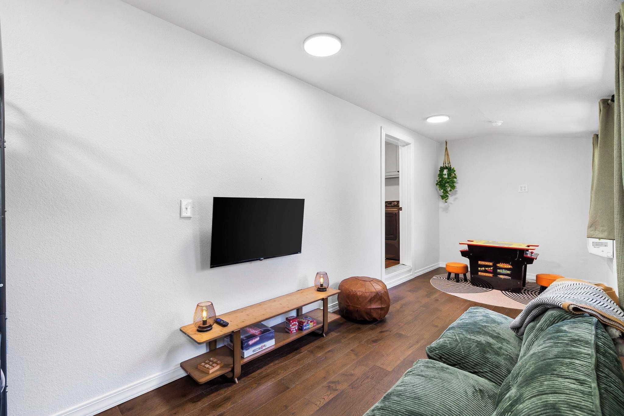 A living room with a flat-screen TV mounted on the wall, a wooden bench with storage underneath, a green sofa, and a small table with a plant.