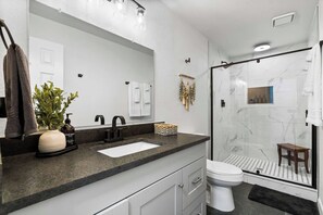 Ein modernes Badezimmer mit großem Spiegel, Waschbecken, Toilette und einer Duschkabine aus Glas.