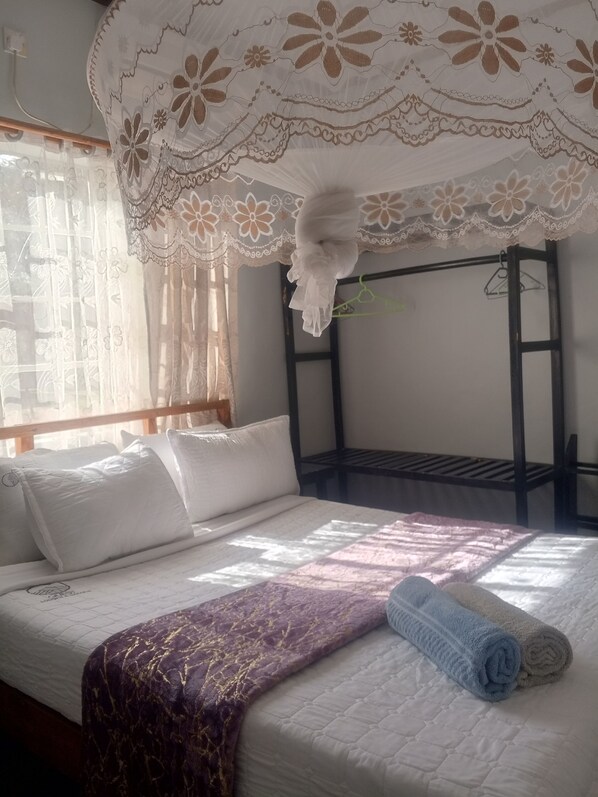 A bed with white bedding, a purple blanket, and rolled towels. - Quest Lodges and Safaris (Lilongwe)