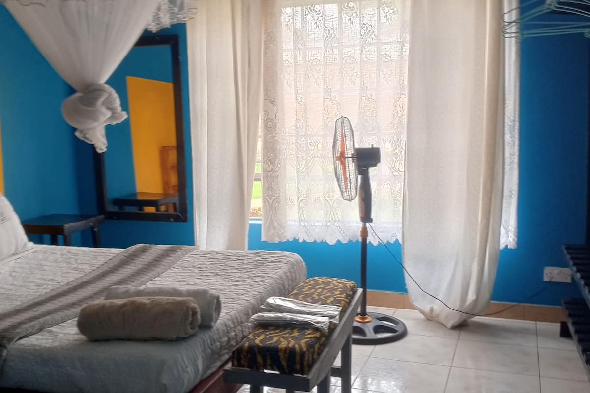 Quarto com cama, mesa de cabeceira e ventilador.