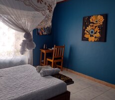 Un dormitorio con cama, una silla, una mesa con hervidor y un cuadro en la pared.