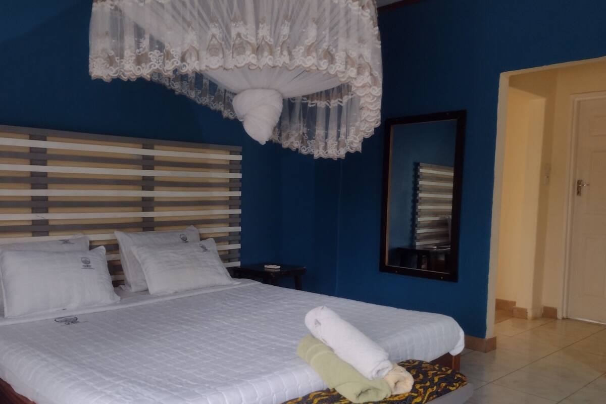 Quarto de hotel com uma cama, mesa de cabeceira, espelho e porta.
