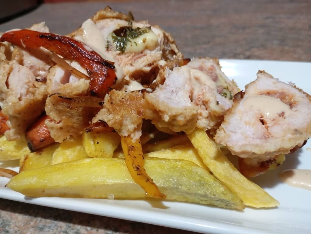 Un plato de comida con pollo a la parrilla, papas y pimientos rojos.