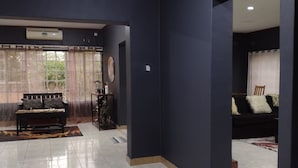 A spacious living area with a dark blue wall, a sofa, a coffee table, and a large window with sheer curtains. - Quest Lodges and Safaris (Lilongwe)