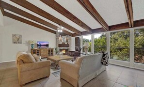 A spacious living room with a fireplace, large windows, and a stone accent wall.