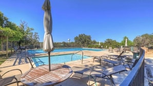 A swimming pool with lounge chairs and umbrellas, surrounded by trees and a clear sky.