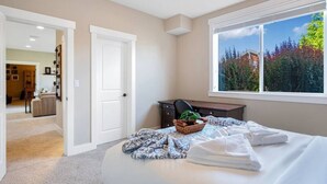 A bedroom with a large bed, a window with a view of trees, a desk with a chair, and a door leading to another room. - 2BR Hideaway: Bar Vibes, Game & LEGO Joy @Bellevue (Bellevue)