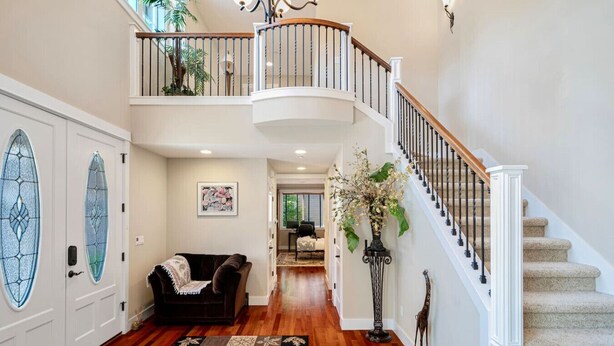 A spacious foyer with a wooden floor, a black leather sofa, a decorative rug, a staircase with a white railing, and a large window with a view of the outdoors. - Stylish Bellevue 5BR/2.5BA Upper Unit | LEGO Fun! (Bellevue)