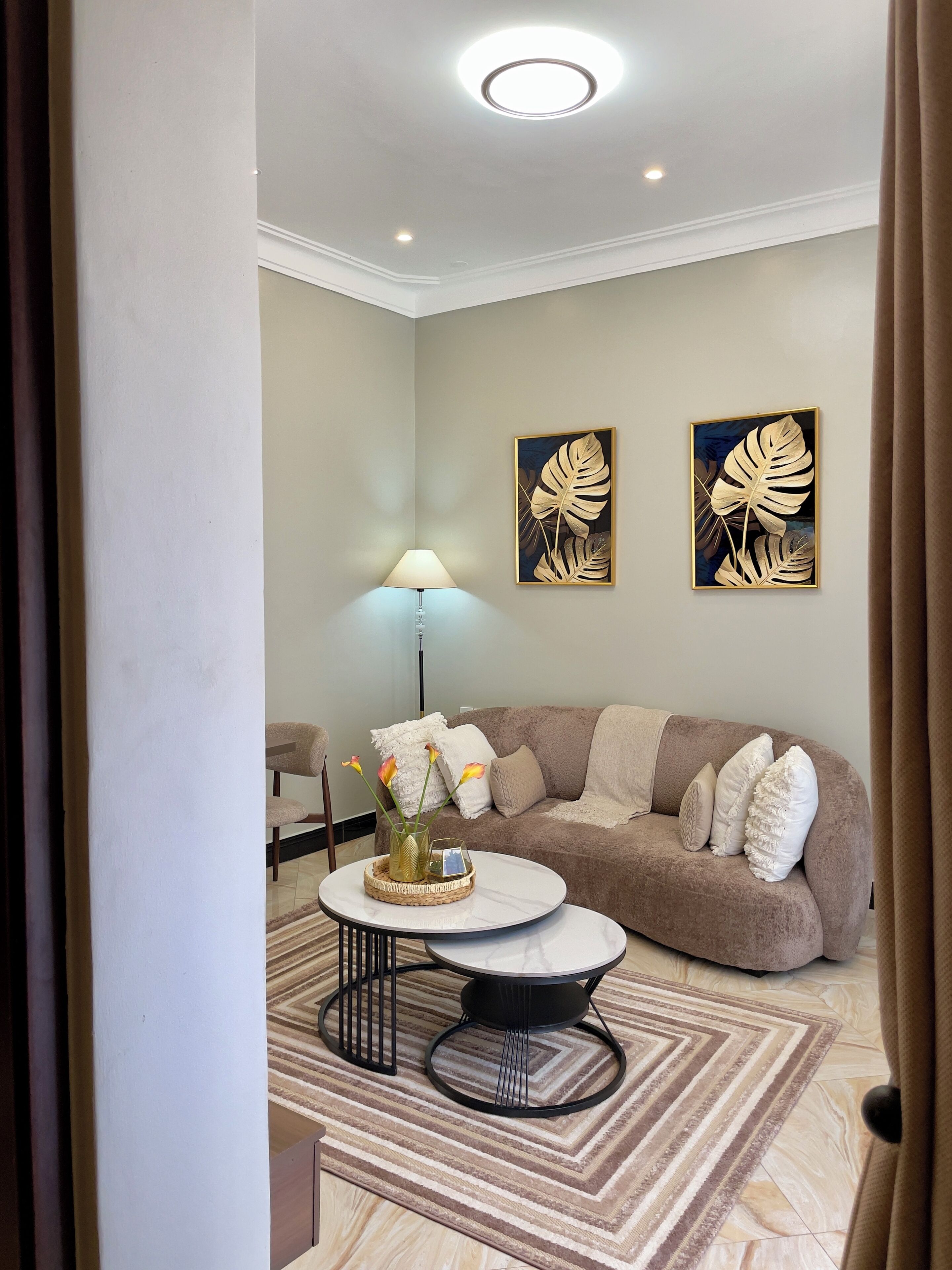 Una sala moderna con un sofá beige, una mesa de centro redonda y dos obras de arte con forma de hojas colgadas en la pared.