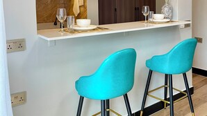 Una cocina moderna con encimera blanca, armarios de madera y dos taburetes de color turquesa.