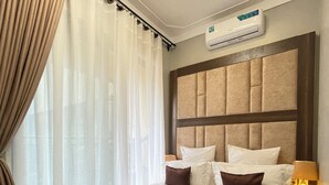 Una habitación de hotel con una cama grande, cabecera, mesita de noche con lámpara y equipo de aire acondicionado.