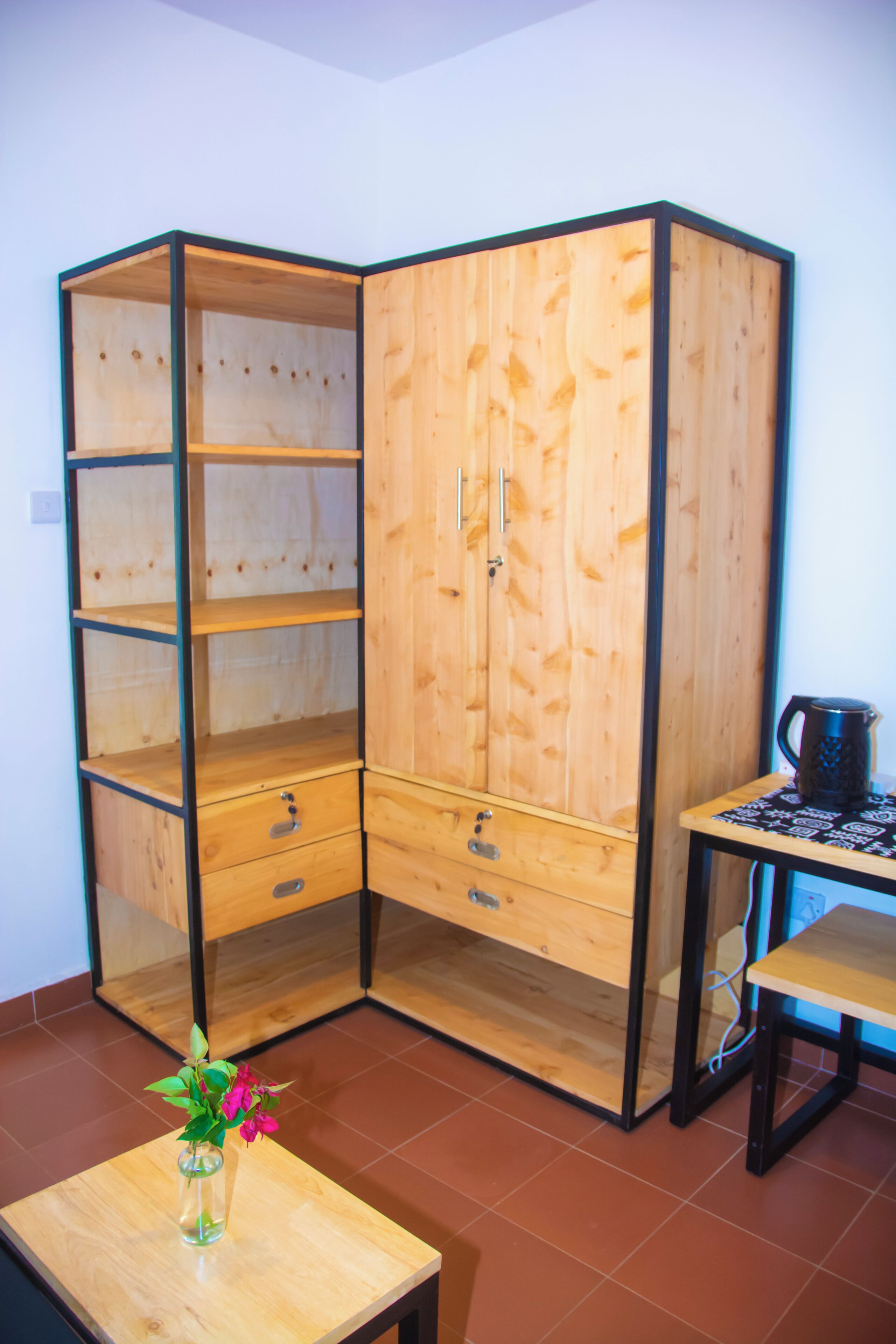 Una habitación de esquina con un armario de madera, una mesita con un jarrón y piso de baldosas.