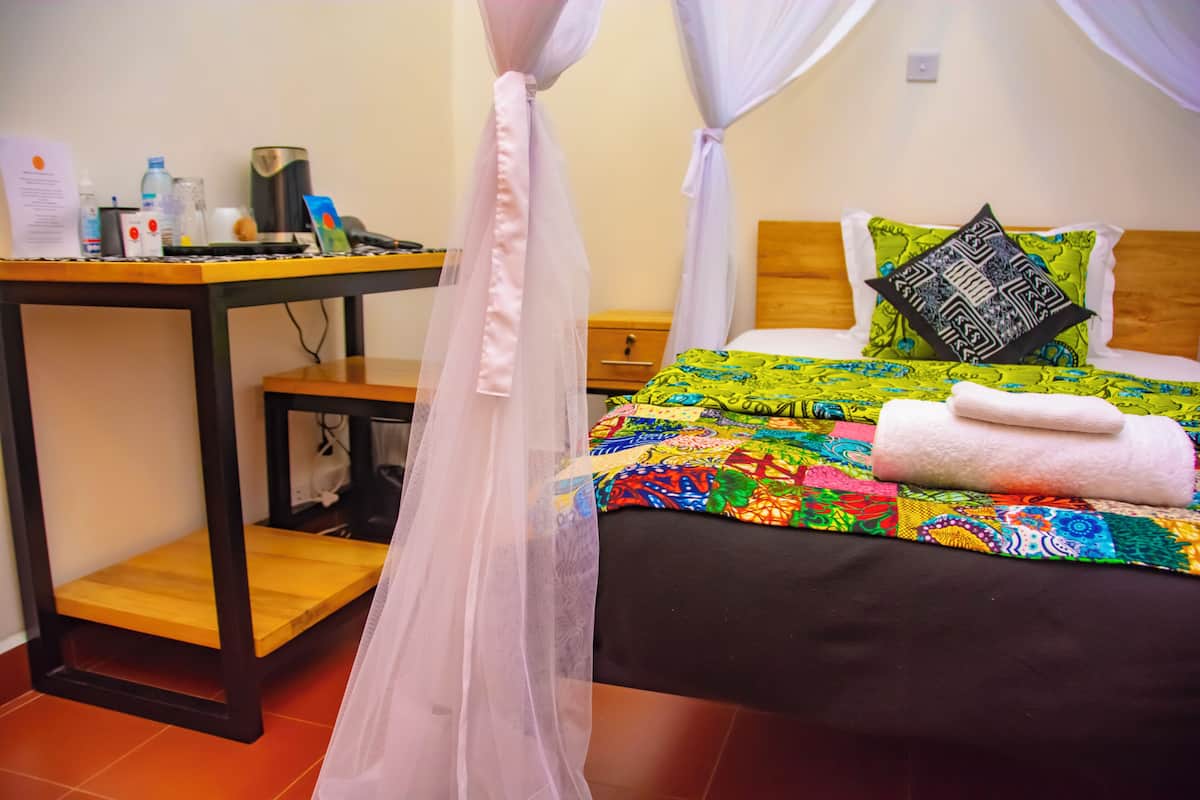 Una habitación con una cama, una mesita de noche y un dosel contra mosquitos, además de una colcha colorida.