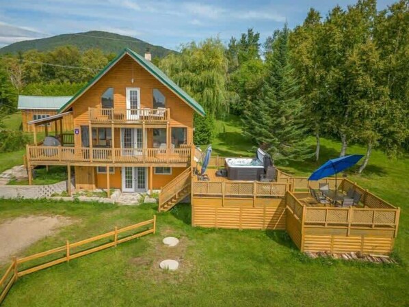 A two-story wooden cabin with a deck, outdoor seating, and a hot tub. - Spa, Pool table, Mountain view | Martine-54 (Petite-Rivière-Saint-François)