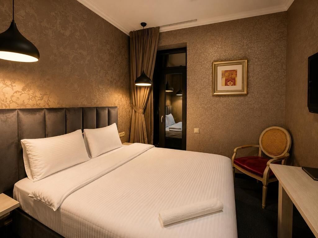 Hotellihuone, jossa on suuri sänky, työpöytä, tuoli, seinällä oleva kehystetty kuva ja ovi, joka johtaa toiseen huoneeseen.