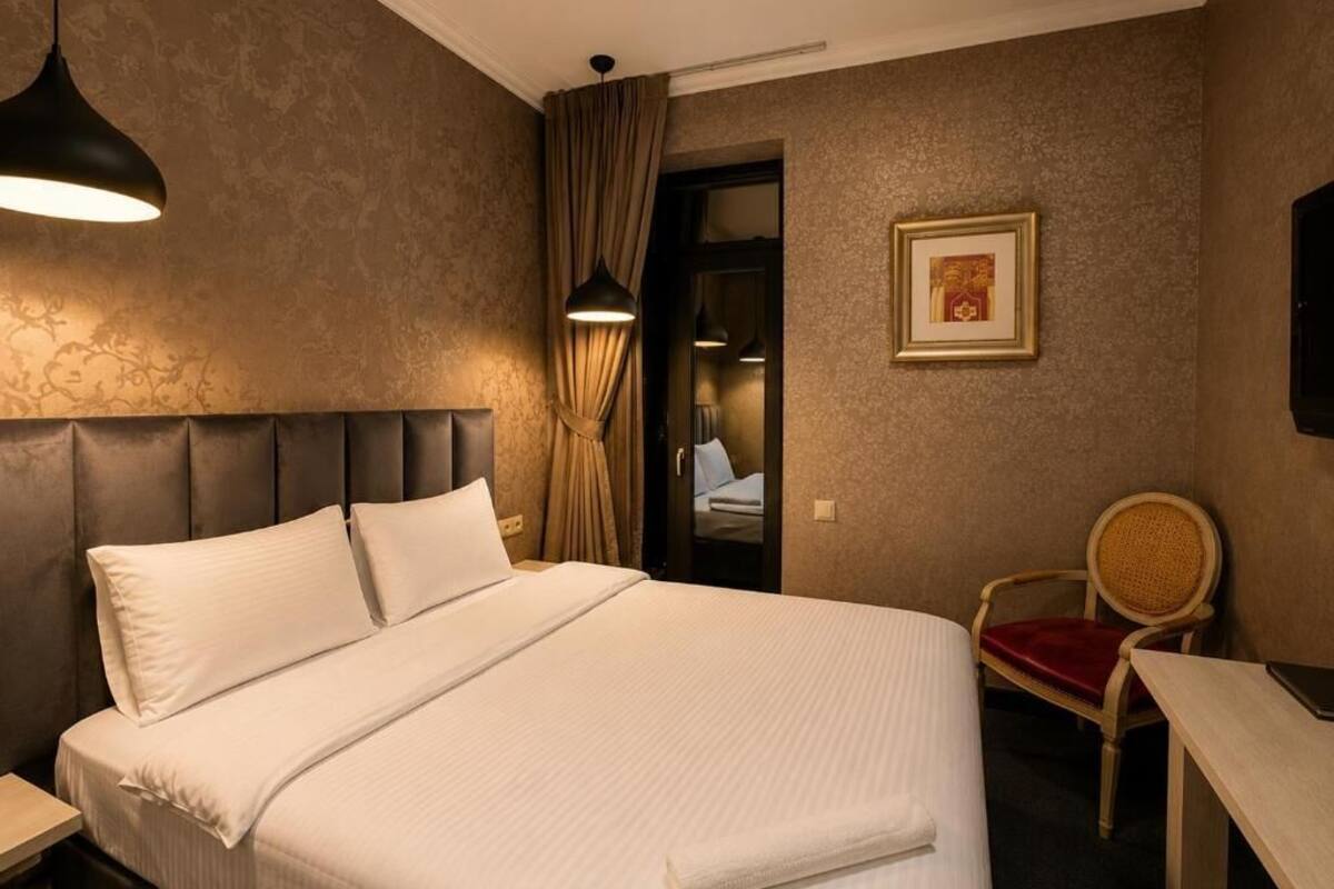 A hotel room with a large bed, a desk, a chair, a framed picture on the wall, and a door leading to another room.