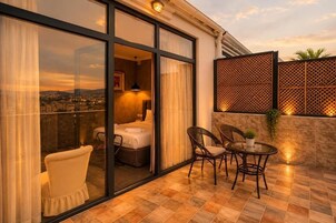 A hotel room with a glass door, a bed, a chair, a table, and a view of the cityscape.