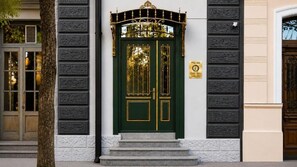 A green door with gold accents, flanked by white and black textured walls, and a small plaque above the door. - Hotel Day Inn (Tbilisi)