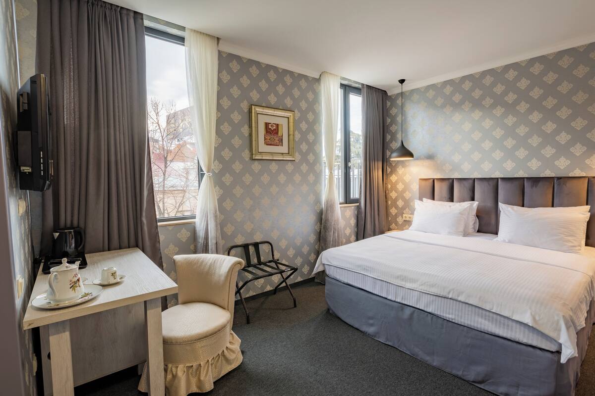A hotel room with a bed, a desk with a coffee maker, a chair, a television, and a framed picture on the wall.