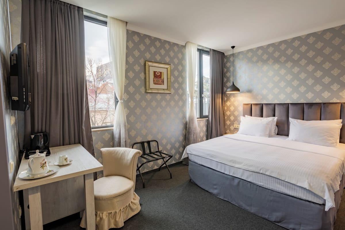 Hotellihuone, jossa on sänky, työpöytä, kahvinkeitin, tuoli, televisio ja seinällä kehystetty taulu.