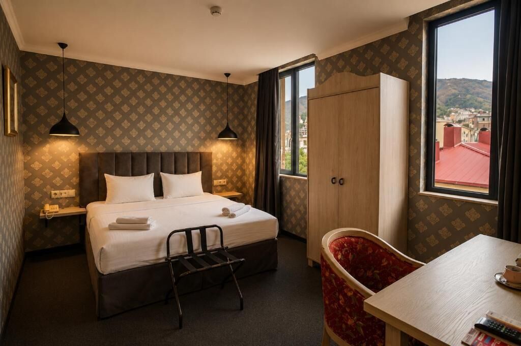 Hotellihuone, jossa on sänky, yöpöydät, työpöytä, tuoli, vaatekaappi ja ikkuna, josta on näkymä.