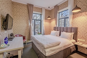 Hotellihuone, jossa on sänky, työpöytä tuolilla, puhelin ja ikkuna, jossa on verhot.