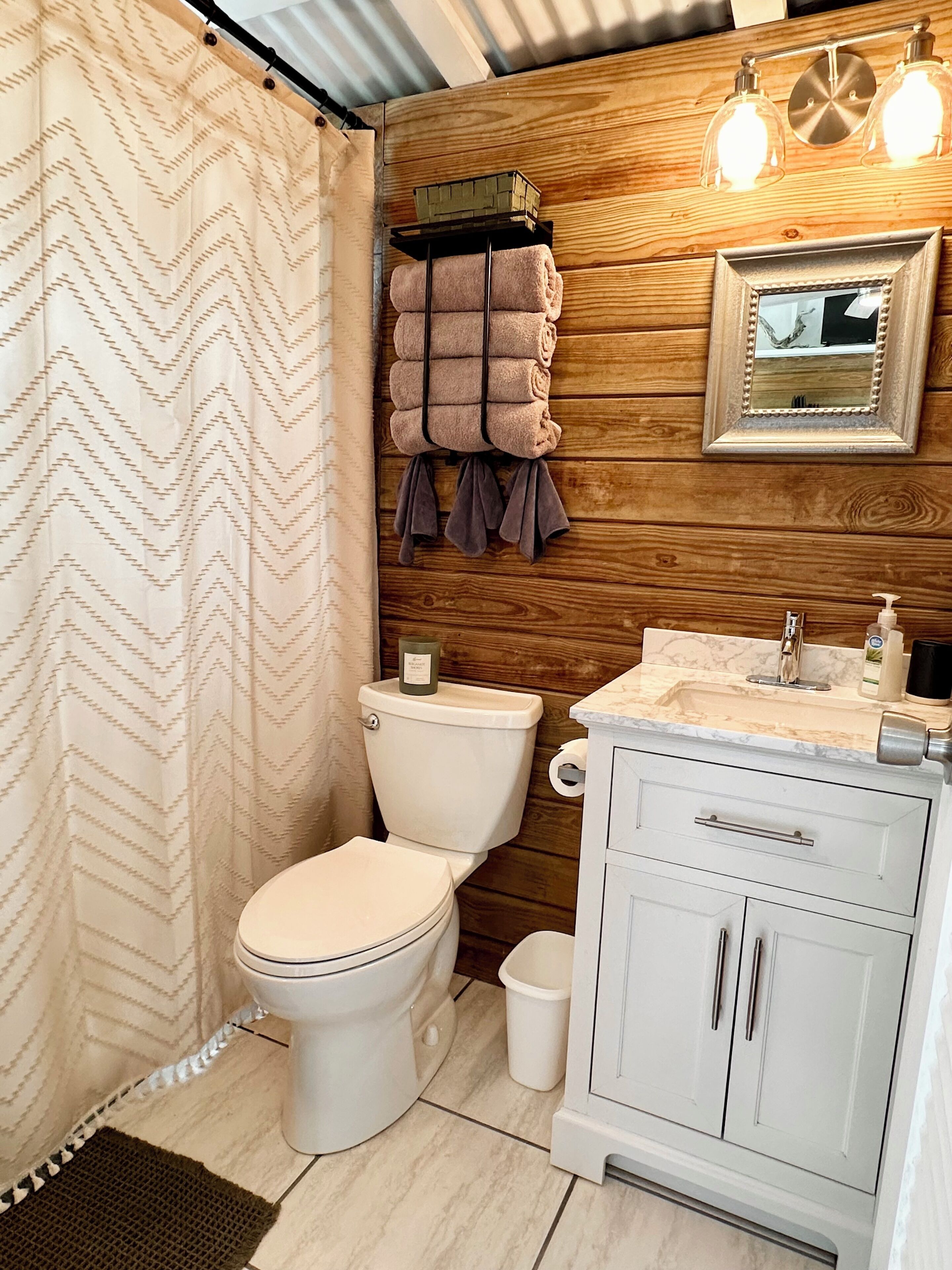 Ein Badezimmer mit Toilette, Holzvertäfelung, Waschbecken mit Spiegel und Handtüchern an der Wand.