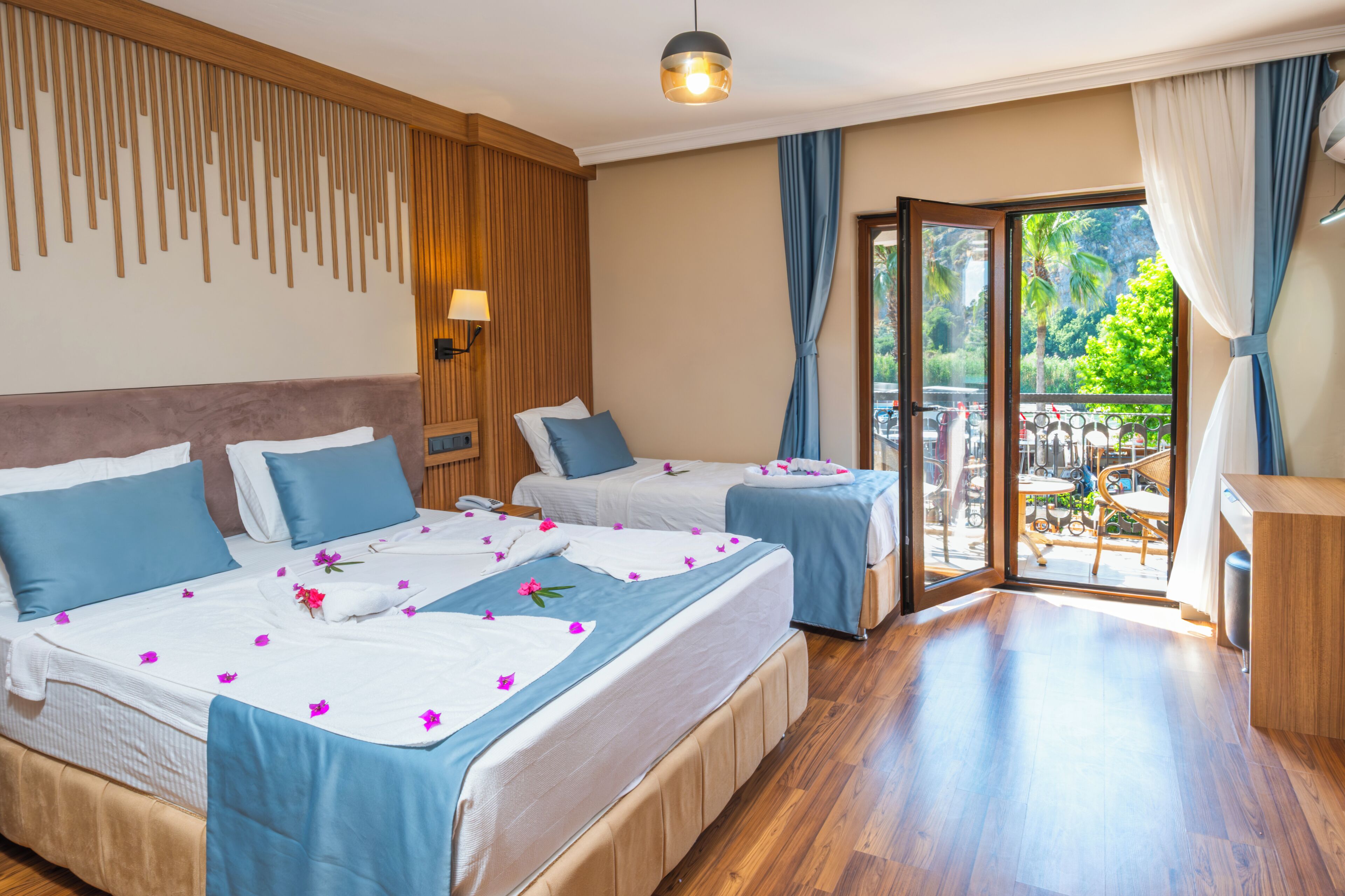 A hotel room with two beds, a wooden headboard, a balcony with a view, and a wooden floor.