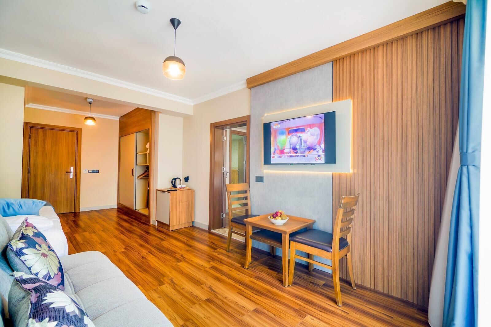 Una sala moderna con piso de madera, un sofá, un televisor montado en la pared y una mesita con un frutero.