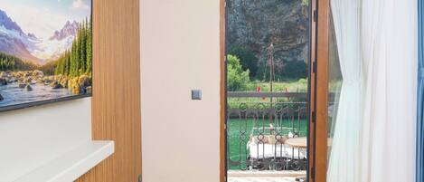 A room with a large TV on the wall, a sliding glass door leading to a balcony with a boat and greenery.
