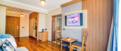 A modern living room with a sofa, a dining table with chairs, a TV mounted on the wall, and a wooden cabinet.