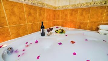 A bathtub with rose petals, a bottle of wine, and two glasses.