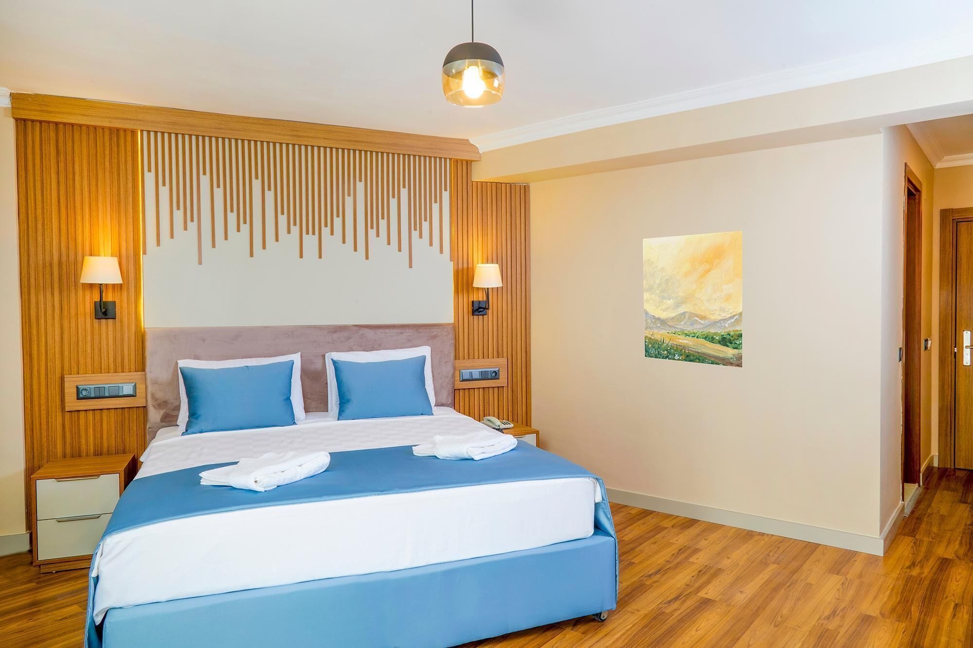 Une chambre d’hôtel avec un grand lit, un mur lambrissé en bois, deux lampes de chevet, un tableau et un plancher en bois.
