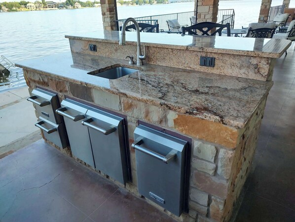 An outdoor kitchen with a sink, built-in cabinets, and a stone countertop.