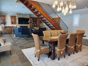 Un vaste salon agrémenté d’un escalier en bois, un coin repas avec des chaises en osier et une cuisine à l’arrière-plan.