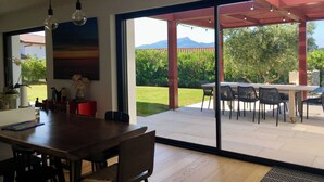 An open-plan living area with a dining table and chairs, a large sliding glass door leading to an outdoor patio with a table and chairs, and a view of a mountain in the distance.