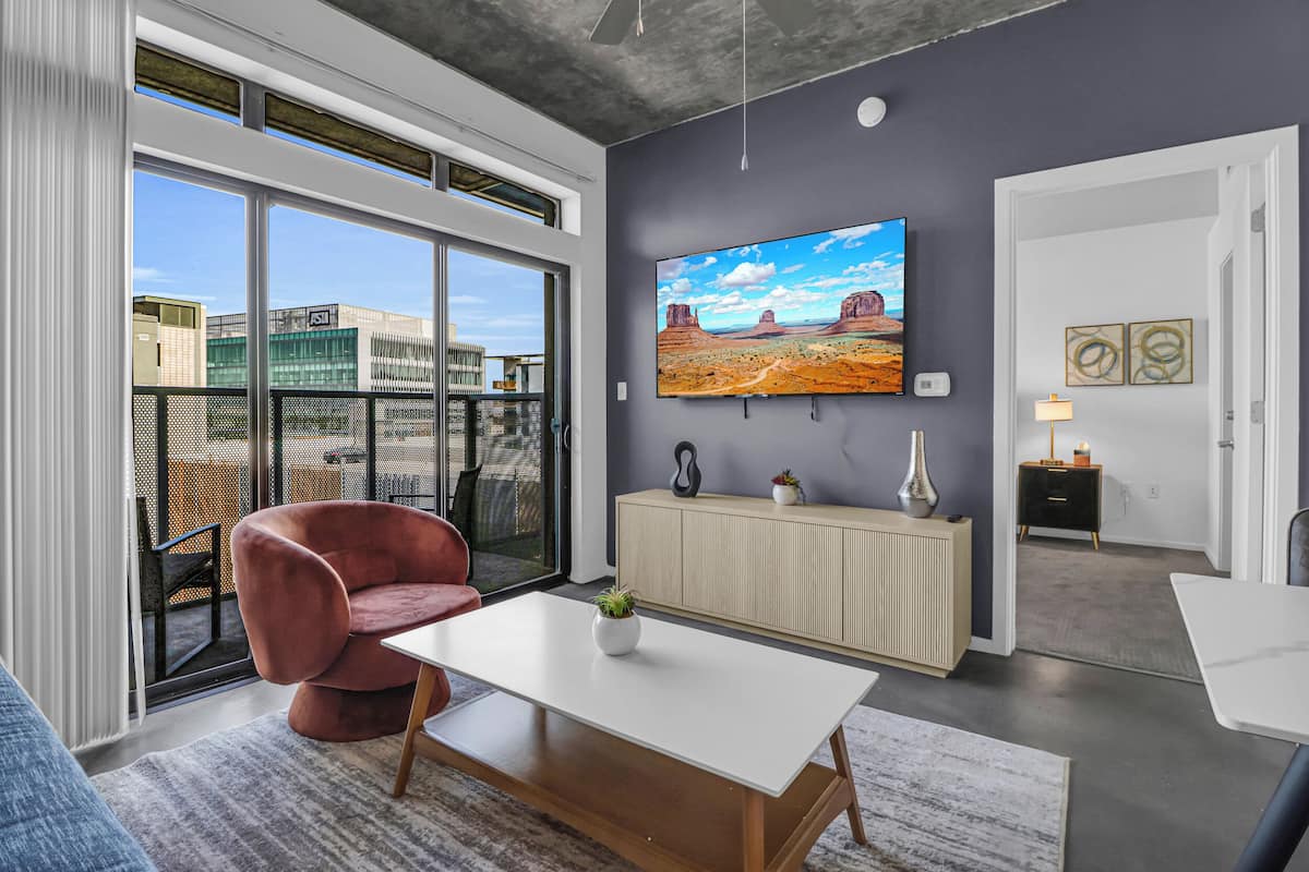 Ein modernes Wohnzimmer mit einem großen Fenster, einem roten Sessel, einem weißen Couchtisch und einem an der Wand befestigten Fernseher.