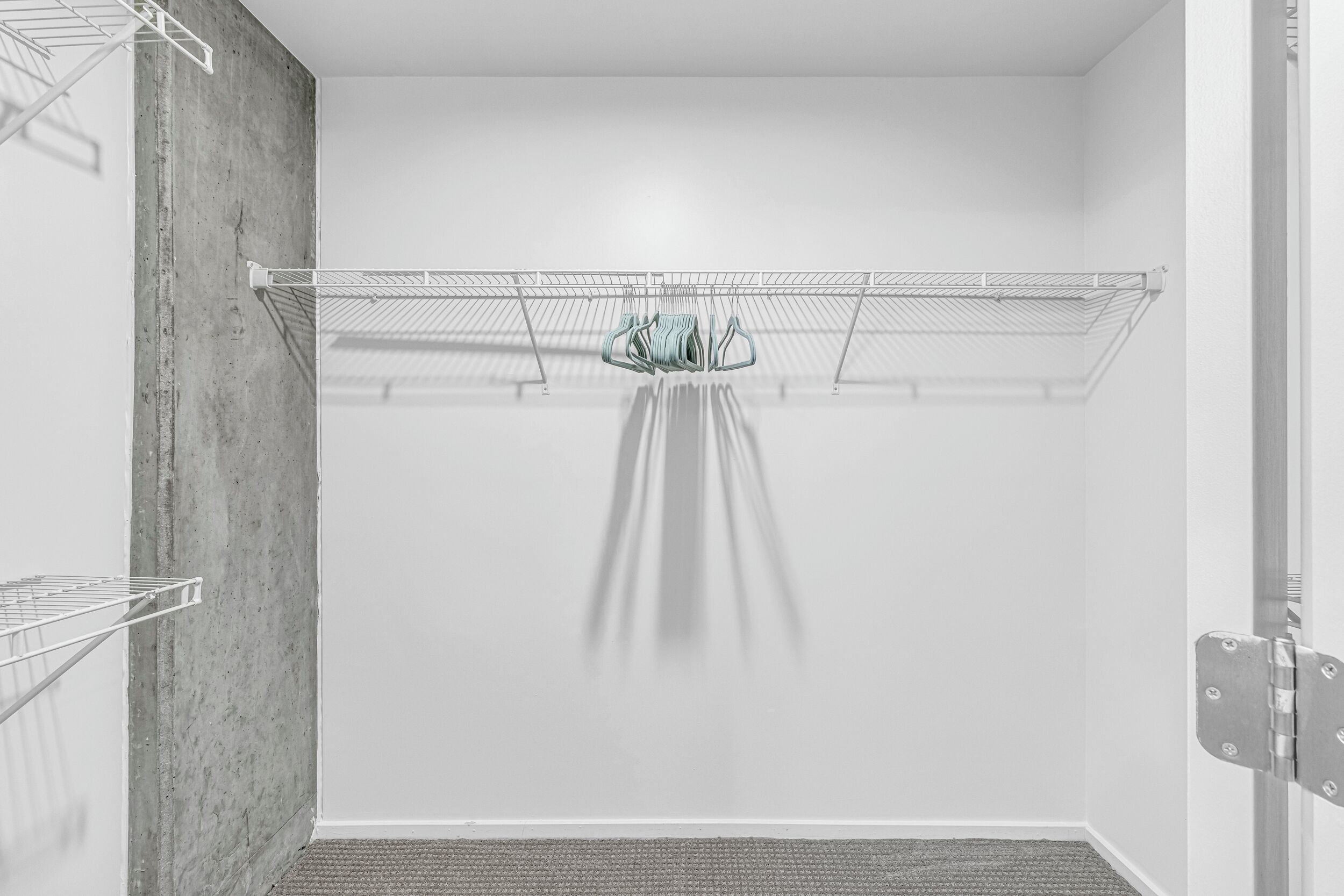 Ein Zimmer mit einem Drahtregal an einer Betonwand, einer Tür mit Metallgriff und einem Teppichboden.