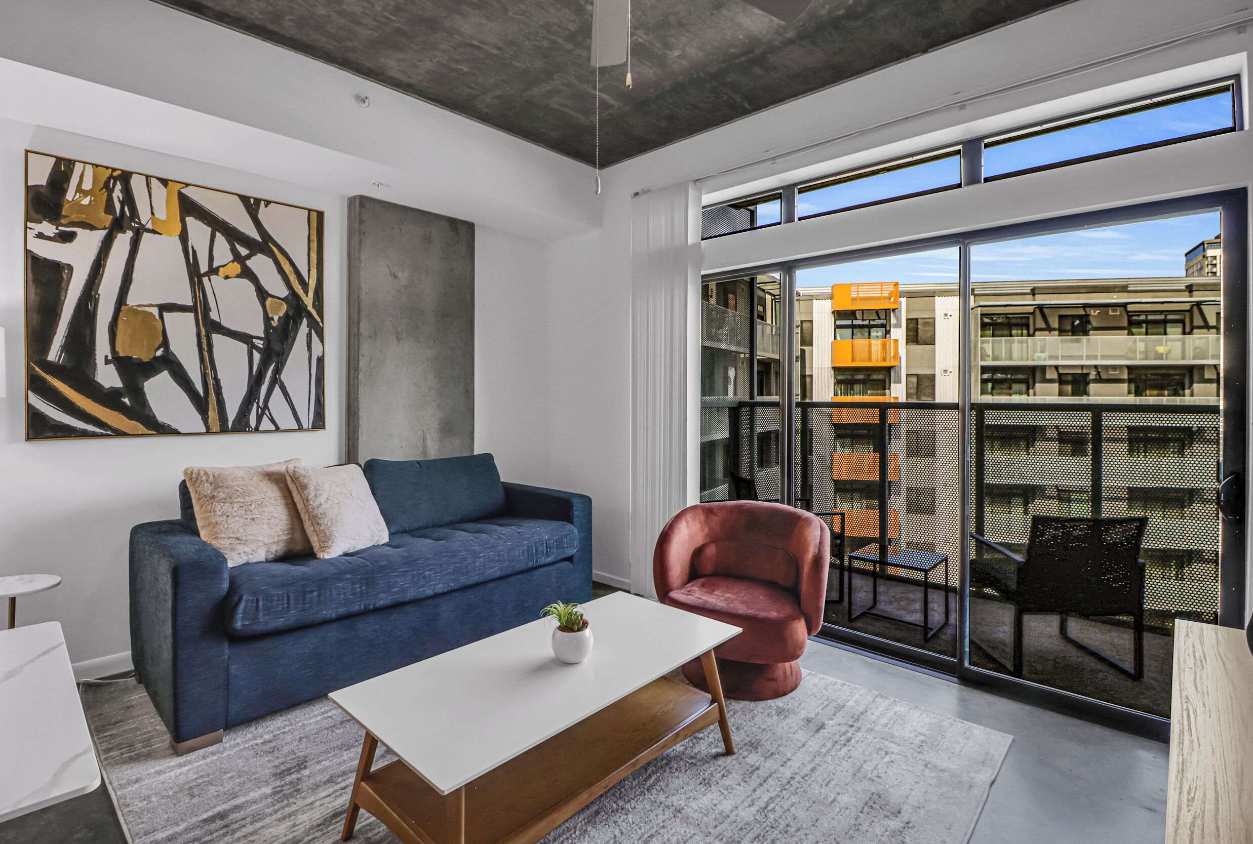 A modern living room with a blue sofa, a red chair, and a white coffee table.