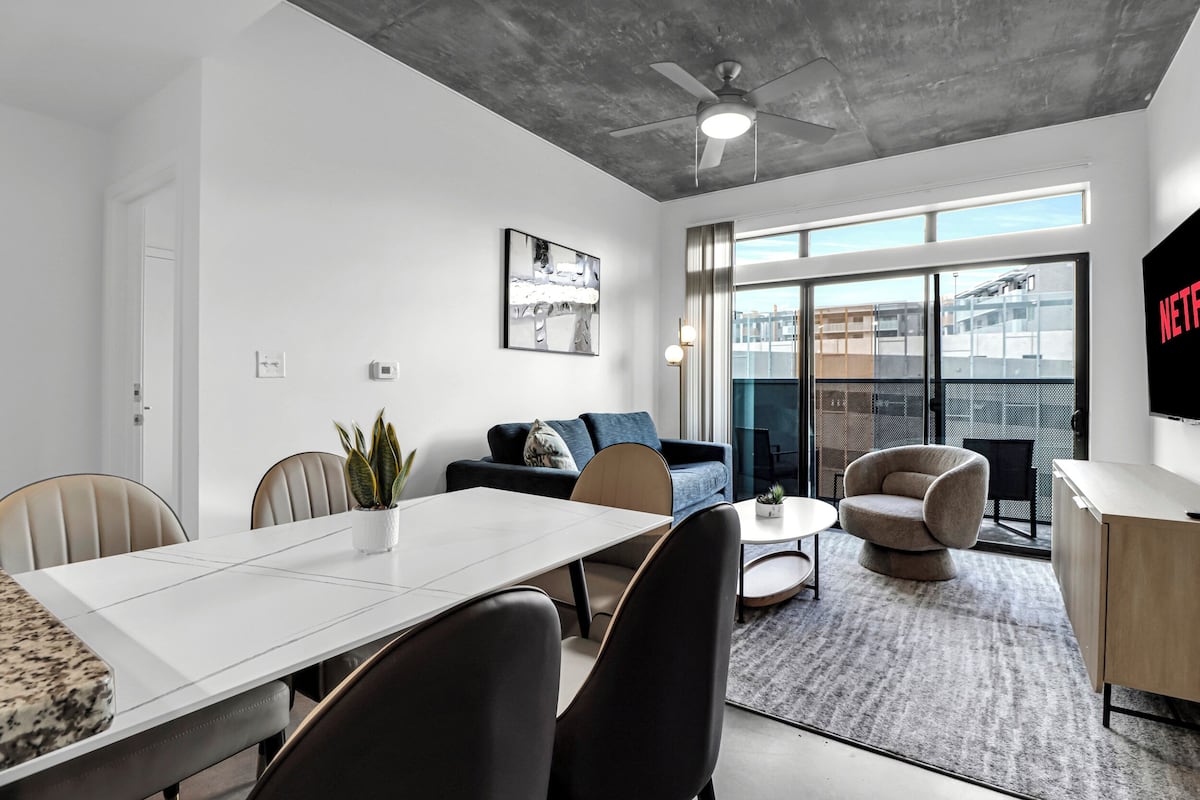 Ein modernes Hotelzimmer mit Essbereich, einer Couch, einem Sessel, einem Fernseher und einem großen Fenster mit Blick auf die Stadt.