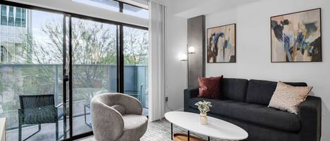 A modern living room with a sofa, armchair, and coffee table, large windows, and abstract art on the wall.