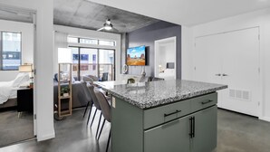 Une cuisine moderne dotée d’un comptoir en granit, d’un ventilateur de plafond et d’un téléviseur fixé au mur.