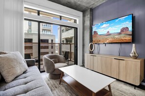 A modern living room with a sofa, armchair, and coffee table, a television mounted on the wall, and a view of the city through large windows. - Phoenix Urban Luxury Escape (Phoenix)