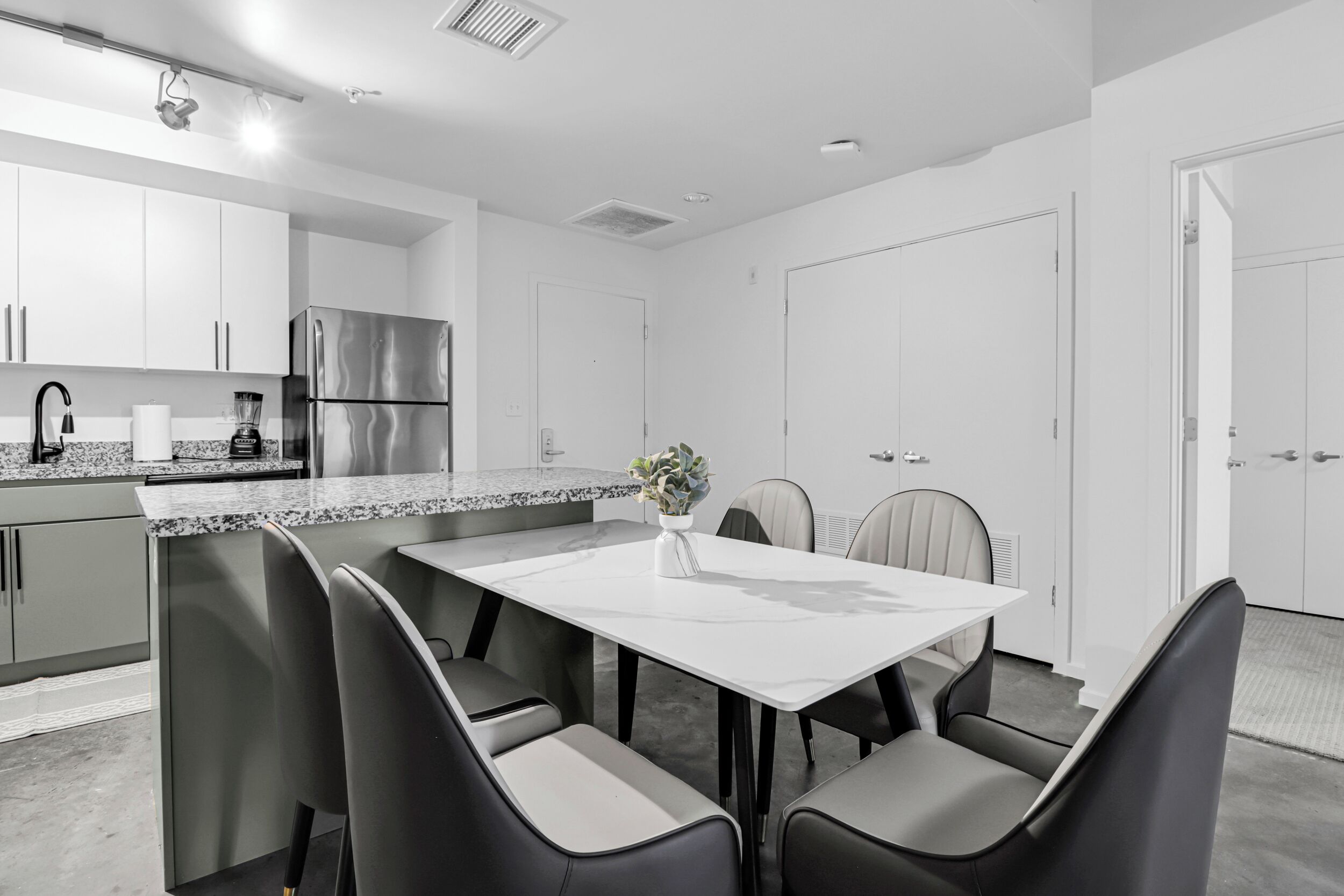 Een moderne keuken met een centraal eiland, inbouwapparatuur en een eethoek met een witte tafel en stoelen.
