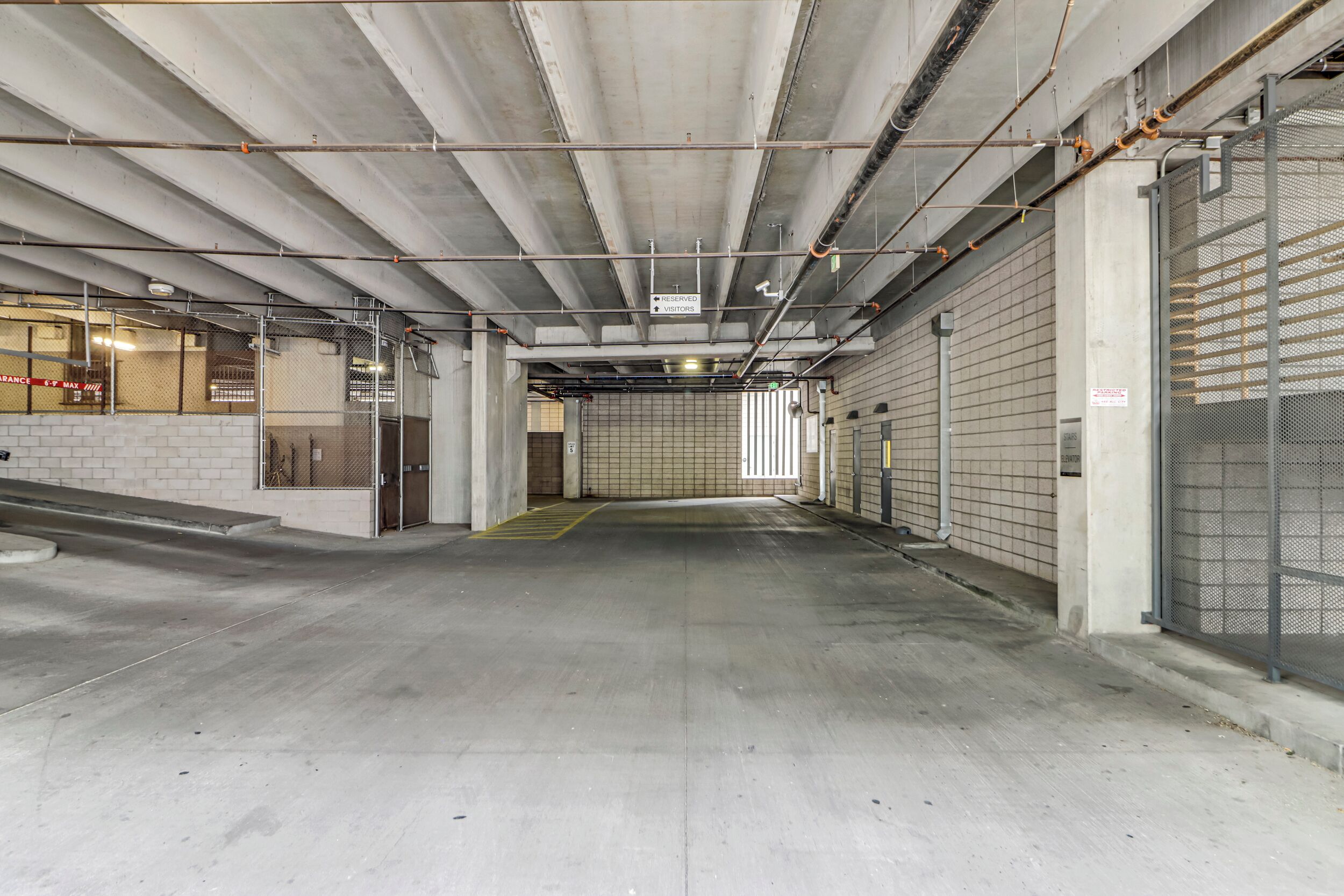 Un parking souterrain vide, avec des planchers et des murs en béton, des escaliers en métal et quelques portes visibles.