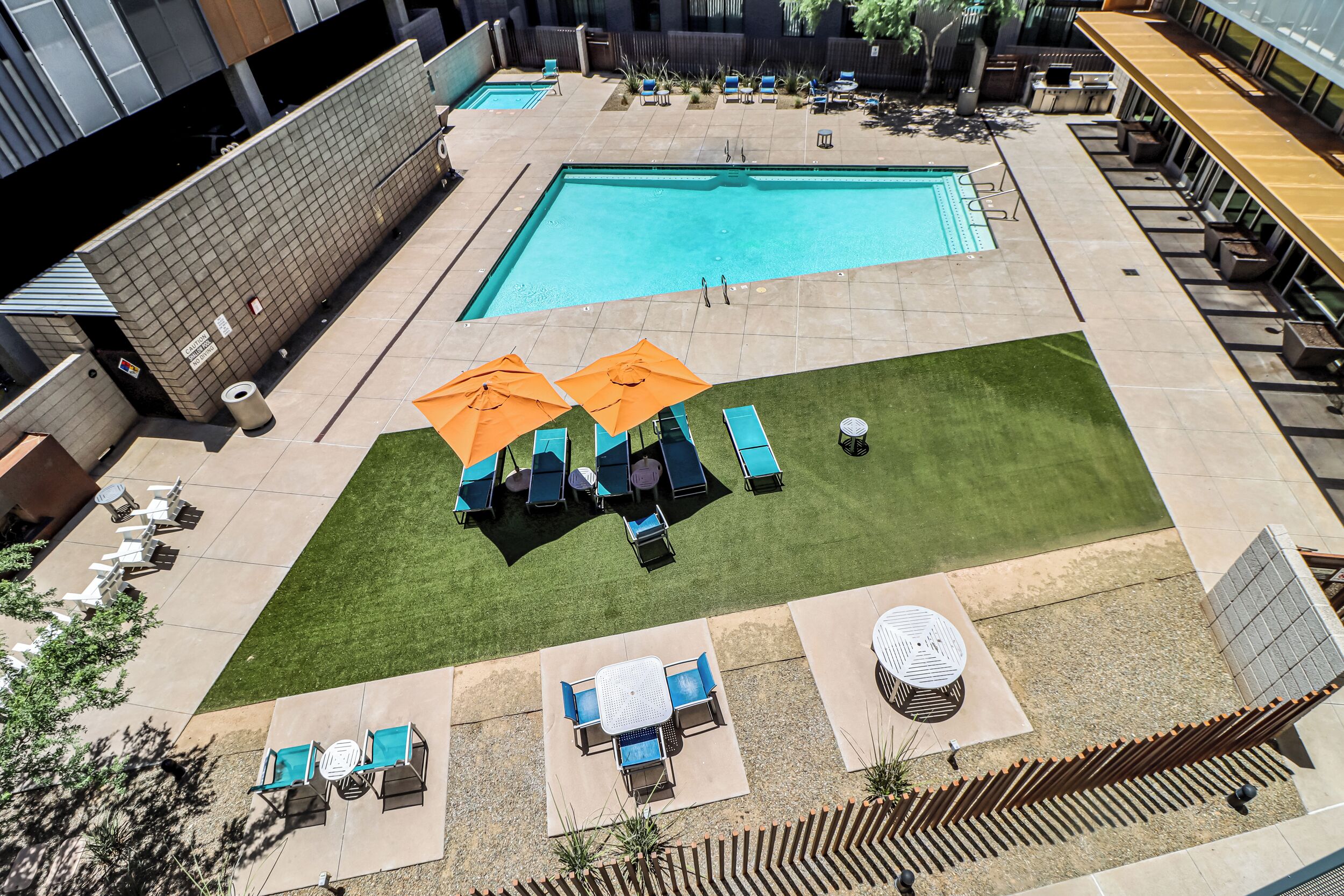 A rooftop pool area with two pools, lounge chairs, and umbrellas.