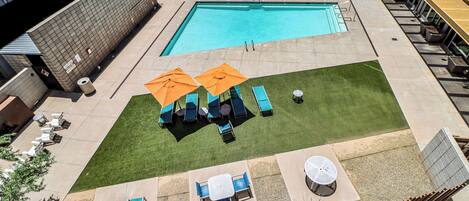 A rooftop pool area with two pools, lounge chairs, and umbrellas.