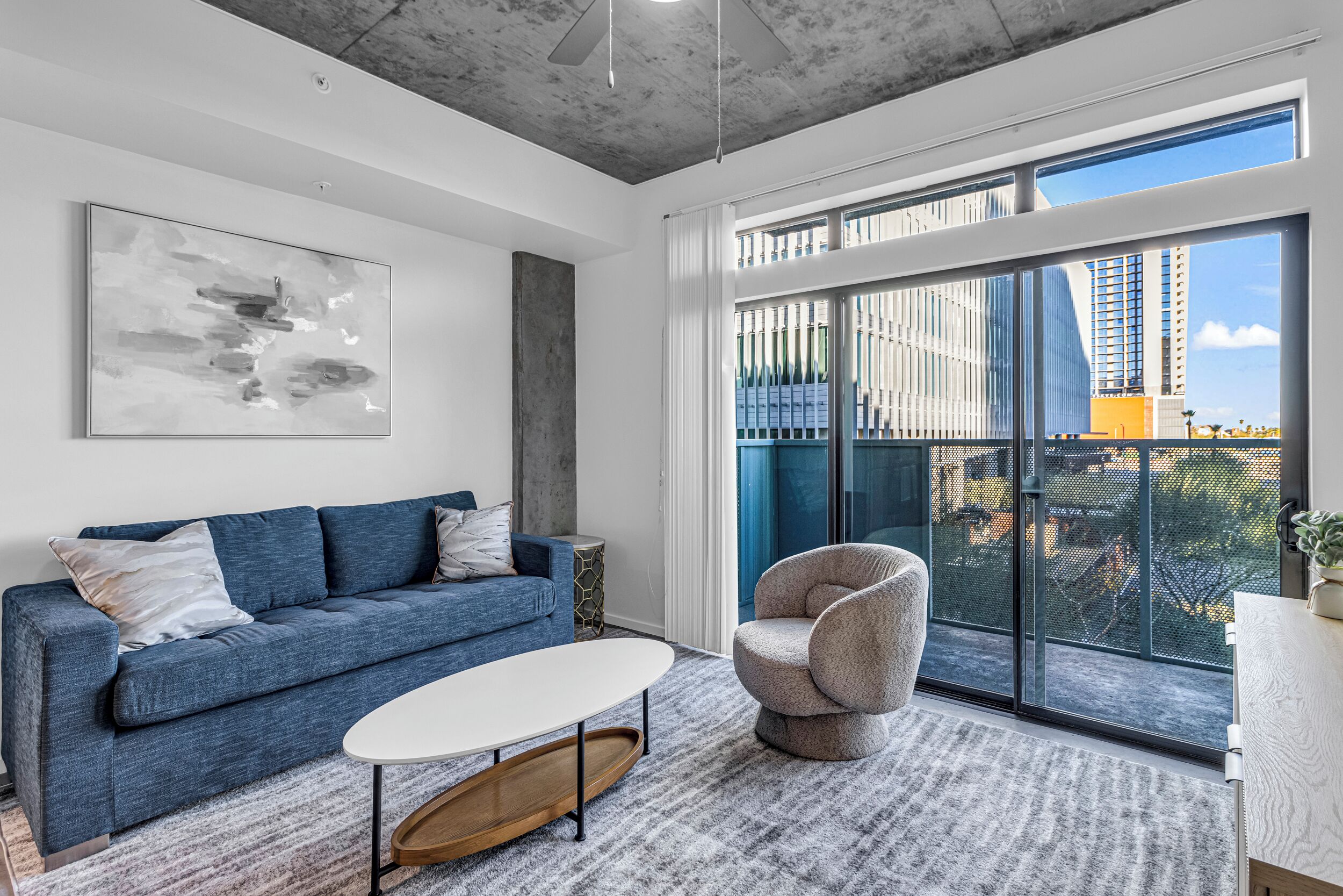 A modern living room with a blue sofa, a white coffee table, and a grey armchair.