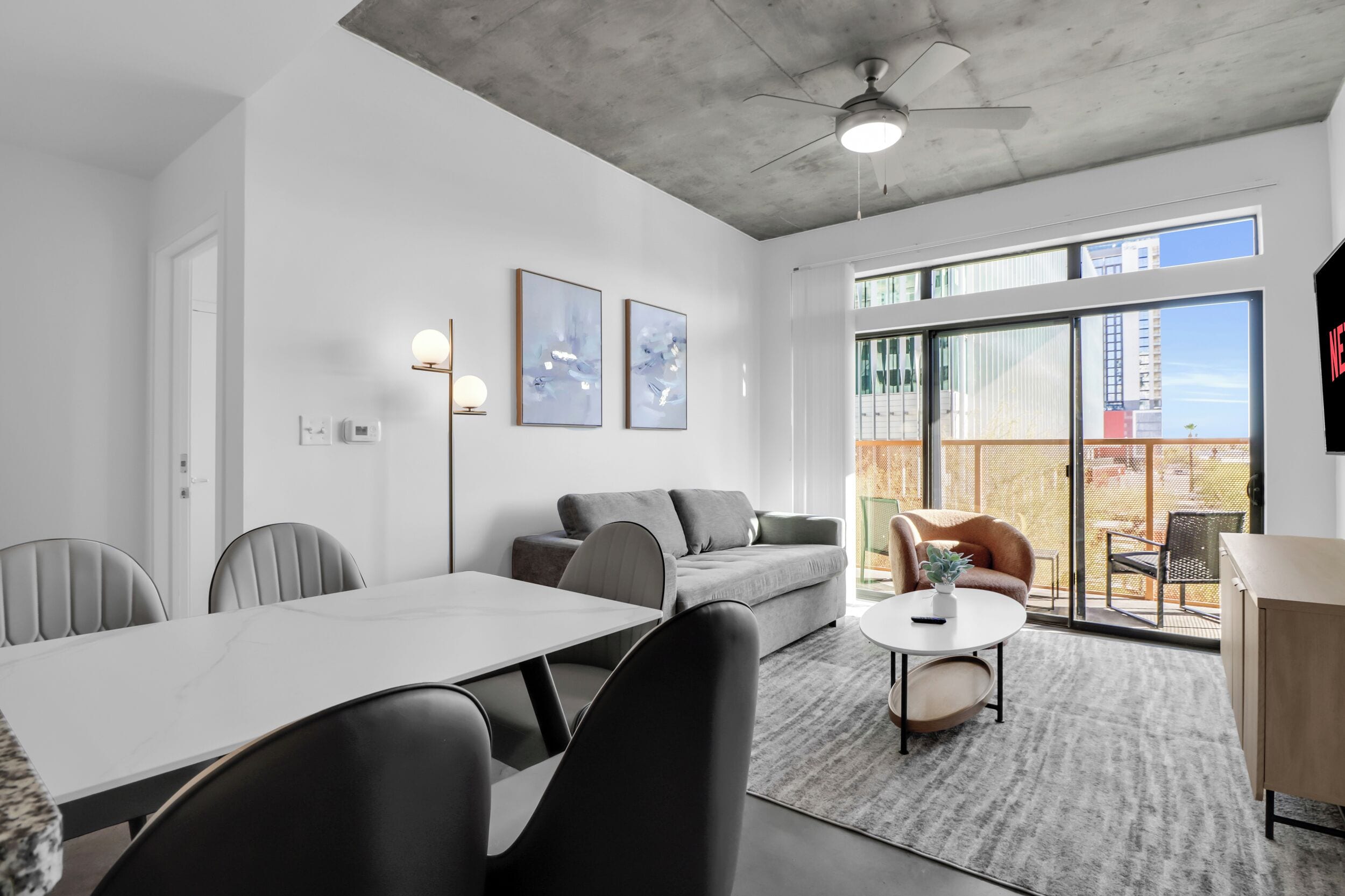 A modern conference room with a white table, black chairs, a grey sofa, and a small round table with a plant.