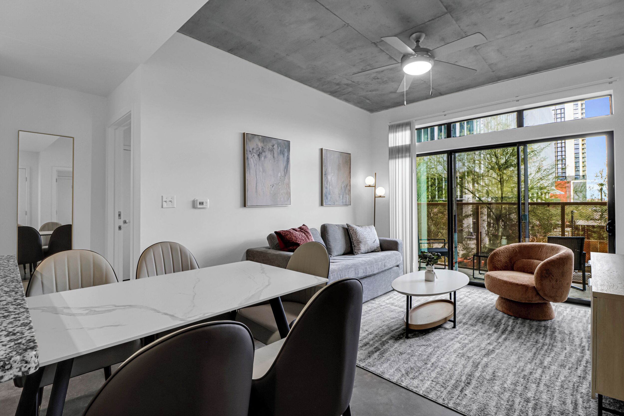 A modern living room with a dining area, large windows, and a ceiling fan.